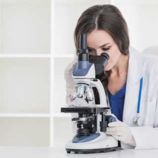 白衣をきている女性が顕微鏡で何かを調べている