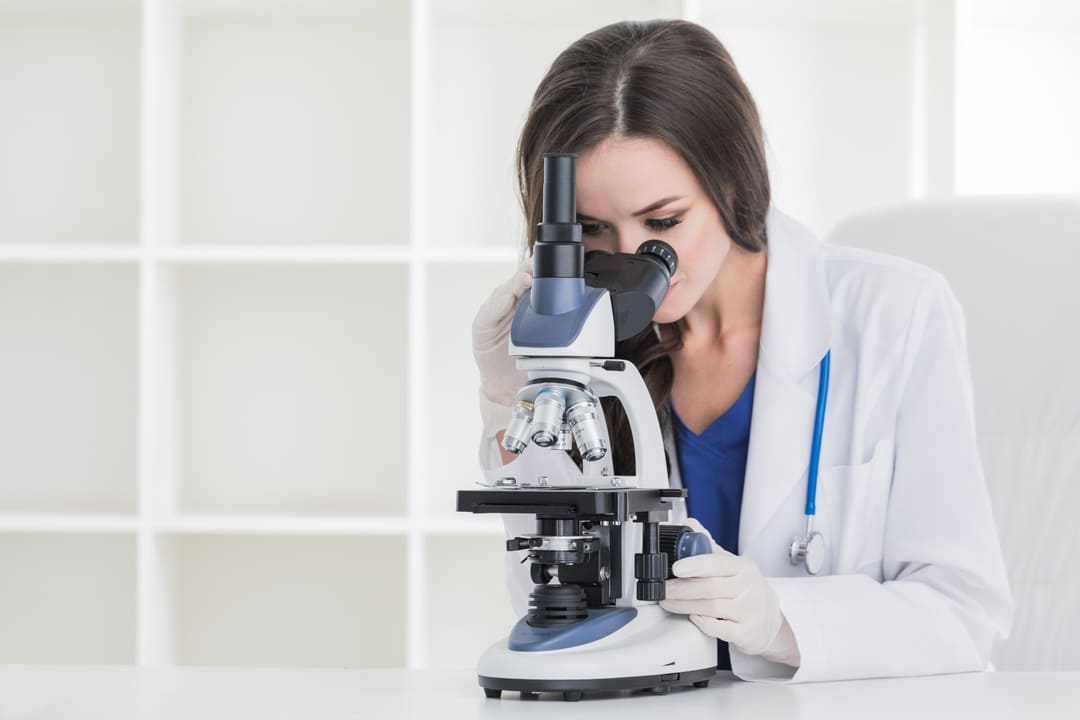 白衣をきている女性が顕微鏡で何かを調べている